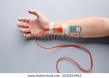 USB charge cable plugged in to a male arm with battery charging symbol. Tiredness, recharging, vitality, endurance, overwork, stamina, fatigue or life energy concept. Royalty-Free Stock Photo #2032810463