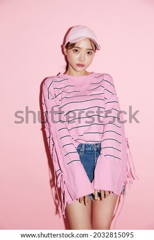 Portrait of casual young Asian woman with cap on pink background.