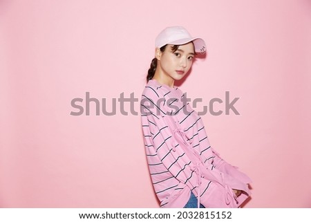 Portrait of casual young Asian woman with cap on pink background.
