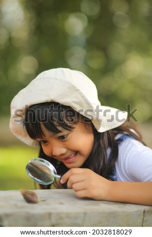 Little kid girl asian wearing a white hat and jeans jumpsuit and xploring nature with a magnifying glass.

Which increases the development and enhances outside the classroom learning skills concept. Royalty-Free Stock Photo #2032818029