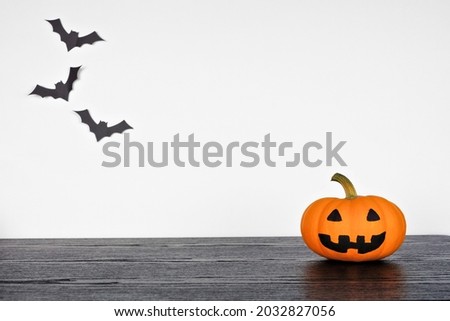 Halloween jack o lantern on a black shelf against a white wall with bats. Copy space.