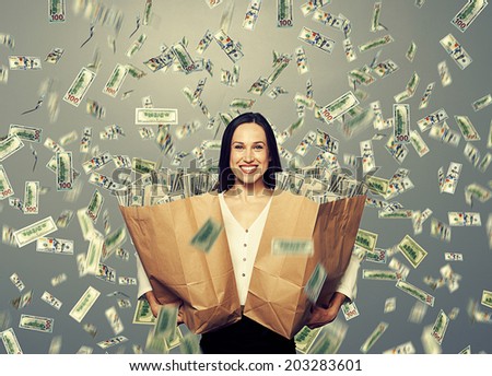 alluring smiley businesswoman holding two paper bags with money under dollar's rain