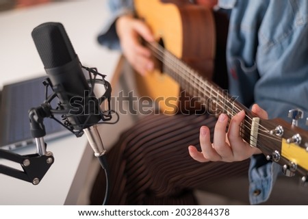 Faceless woman playing guitar and streaming live on laptop.