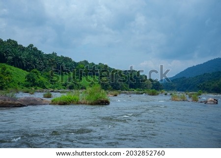Riverscape photography- River flowing under blue sky, Forest and mountains between a cloudy sky and river.