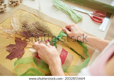 Hands of woman tying ribbon onto dried flower bouquet wen making artwork for room decoration