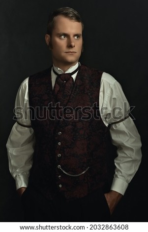 Shadowy portrait of a young man in vintage Victorian attire in front of a dark gray wall. Royalty-Free Stock Photo #2032863608