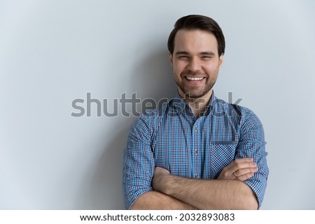 Portrait of happy millennial guy in casual shirt standing isolated by white background with arms folded, looking at camera, laughing, smiling. Studio head shot of 30s confident business man Royalty-Free Stock Photo #2032893083