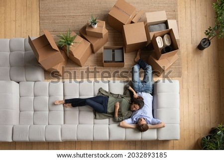 Top above view loving happy young family couple relaxing on huge comfortable couch near boxes with stuff, renewing energy after moving day, enjoying peaceful carefree time together in own apartment. Royalty-Free Stock Photo #2032893185