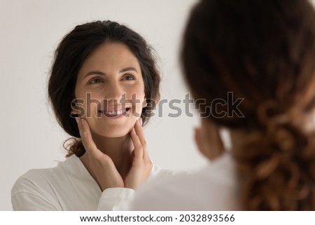 Head shot attractive happy young hispanic latina woman in robe looking in mirror, touching face, enjoying morning evening anti aging skincare routine, feeling satisfied with perfect skin condition. Royalty-Free Stock Photo #2032893566