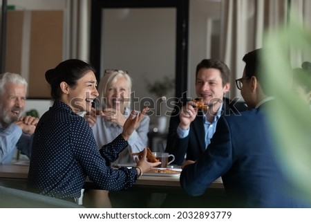 Excited diverse employees eating pizza during break in office together, happy Indian businesswoman laughing at funny joke, talking chatting with colleagues, having fun, sharing corporate lunch Royalty-Free Stock Photo #2032893779