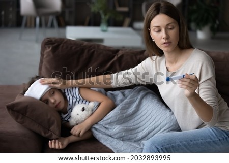 Worried young mother checking body temperature of unhealthy small child daughter using electronic thermometer. Unhappy little kid girl caught cold, having first flu symptoms, feeling unwell at home. Royalty-Free Stock Photo #2032893995
