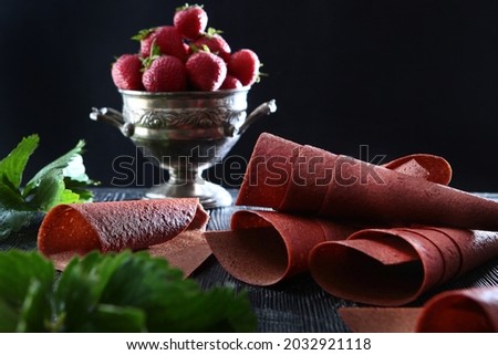 Fresh strawberries in an old metal vase. Natural pastille rolled into a tube. Natural product. Food for vegetarians. Macro photo on a black background. Copy space.