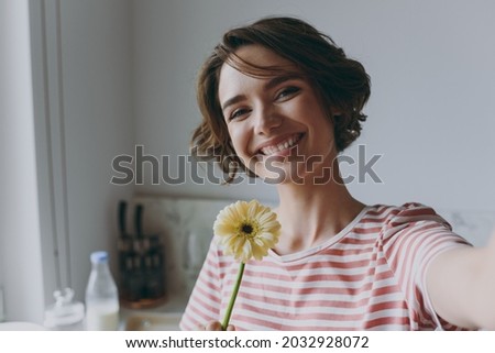 Close up young housewife woman 20s in casual clothes striped t-shirt holding flower gerbera doing selfie shot on mobile phone cooking food in light kitchen at home alone Healthy diet lifestyle concept Royalty-Free Stock Photo #2032928072