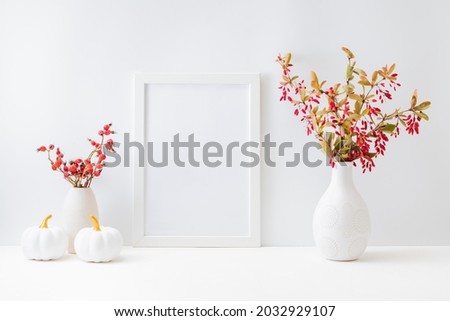 Home interior with decor elements. Mockup with a white frame, colorful autumn leaves and red berries in a vase on a light background
