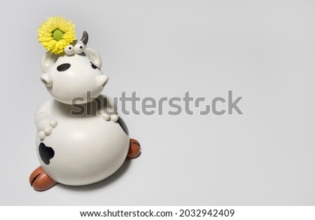 Decorative clay figurine of a funny cow on a white background in a composition with a yellow natural flower. Copy space