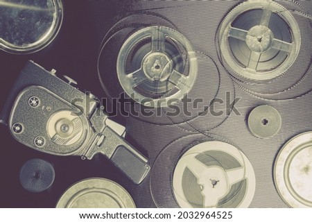 Old amateur movie camera, spools of roll film and reel of film stock on black background