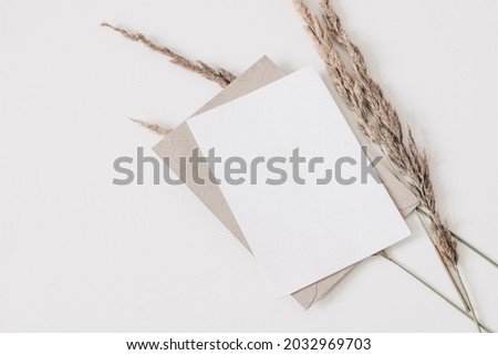 Autumn wedding, birthday stationery composition. Blank greeting card, invitation mockup, craft envelope. Dry grass, festuca plant isolated on white table background. Fall flat lay, top view. Copyspace
