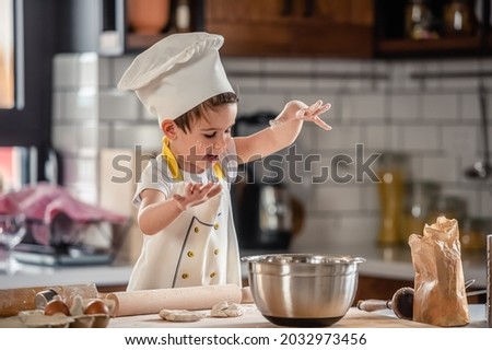 Toddler boy playing with the dough in the kitchen dressed as a chef. Child baking a cake