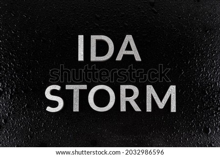the words ida storm laid with silver metal letters over black surface both covered with rain water drops.