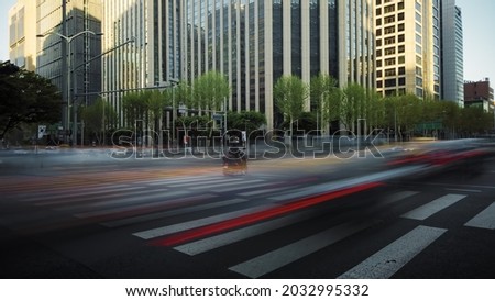 time of a busy crossroad in a big city in the evening. Cars stop at the traffic light and then move forward creating beautiful light trails. Crowds of pedestrians cross the road in their turn.