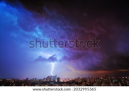 Amazing time of the night storm over the big city, with colorful clouds moving on the sky and bringing first drops of rain, and bright lightnings illuminating the scene.