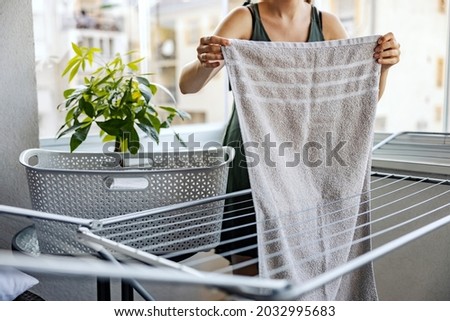 Spread the laundry on the terrace. A woman spreads a washed towel on the rack to dry on the terrace of a sunny day. Housework and apartment and house hygiene. The woman does the housework