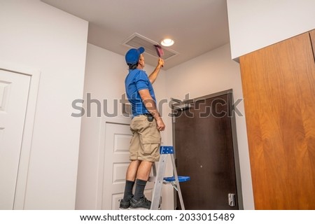 Handyman on a ladder cleaning a return air duct inside of a home Royalty-Free Stock Photo #2033015489