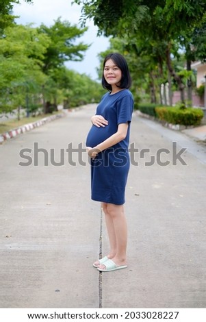 Full body a pregnant mother in a long blue dress is standing  at garden