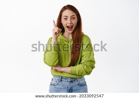 Excited and creative girl student, ginger female model suggest a plan, raise finger eureka sign, pitching an idea, have great solution, standing against white background