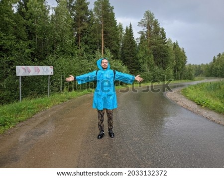 A man in a blue raincoat takes pictures with a smartphone in a autumn rainy forest.