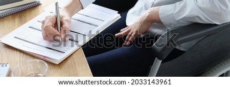 Disabled woman in wheelchair filling out application for employment closeup Royalty-Free Stock Photo #2033143961