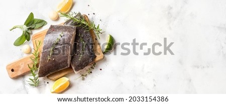 Top view of two raw halibut fish steaks with herbs and lemon on wooden board and white background. Long banner with copy space. Omega 3 fats good for mental clarity. Brain food