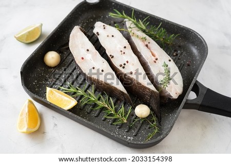 Raw halibut fish steaks with herbs and lemon prepared for cooking in grill pan. Healthy omega 3 unsaturated fats good for brain and mental clarity
