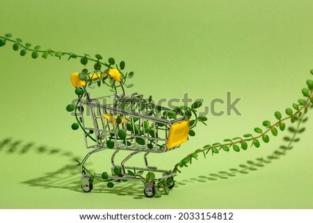 Conscious consumption Zero waste concept. Shopping cart entwined with shoots of plants on green background. Sustainable eco lifestyle. Royalty-Free Stock Photo #2033154812