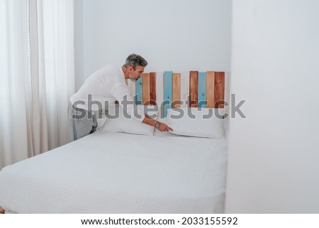 Man in his 50s with gray hair making bed