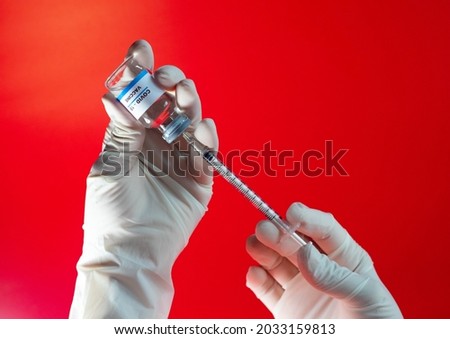 Image of hand holding a syringe pulling the COVID-19 vaccine out of a bottle on a bright red background.