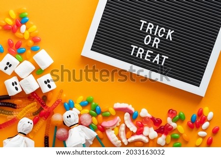 Halloween flat lay composition with sweets, decorations, letter board with sign Trick or Treat on orange background. Flat lay, top view, overhead.