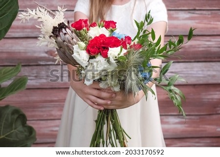 Beautiful girl in a green dress holding a bouquet of flowers and greenery on a wooden background. Copy, empty space for text