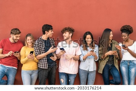 Young friends using mobile smartphone outdoor - Millennial generation having fun with new trends social media apps - Youth technology people addicted - Red background Royalty-Free Stock Photo #2033176214