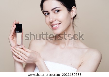 Woman holds Foundation. Photo of pretty woman with perfect skin on beige background. Beauty product presentation