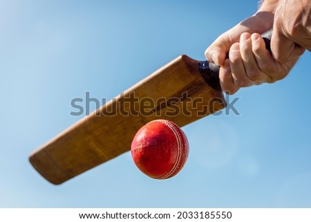 Cricket player batsman hitting a ball with a bat shot from below against a blue sky Royalty-Free Stock Photo #2033185550