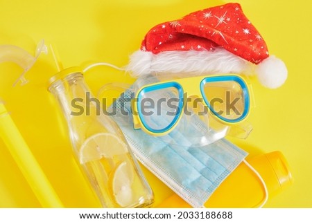 diving set, protective medical mask, santa claus hat, sun cream and a bottle of lemonade on a yellow background, Christmas holidays in a warm country during a pandemic
