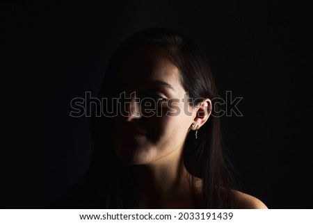 Close-up portrait of a young woman with a positive gaze looking at the camera, on a dark studio background. Happiness concept