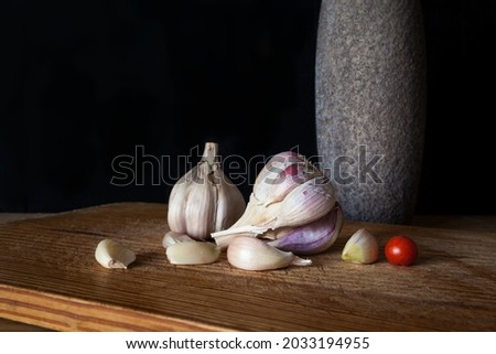 Photograph with black background of two garlic goats and a tomato