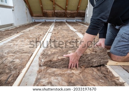 Man insulating the attic with rock wool. Royalty-Free Stock Photo #2033197670