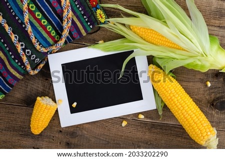 Cobs of ripe raw corn laid on dark wood textured table. White frame with black place for notes. Background, top view, close up, flat lay, copy space.
