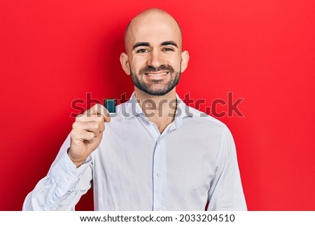 Young bald man holding sdxc card looking positive and happy standing and smiling with a confident smile showing teeth 