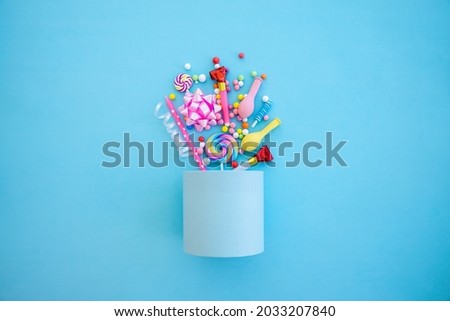 Blue box with various party confetti, balloons, lollipops, candles and decoration on a blue background. Colorful celebration concept.