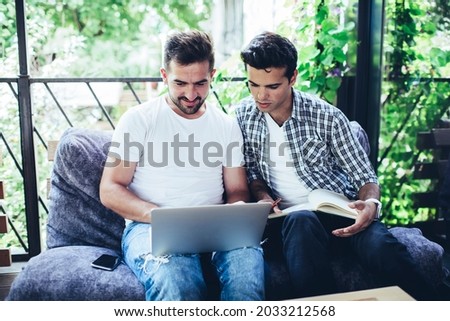 Skilled male students browsing education website while doing homework test discussing received information during together e learning, hipster guys collaborate on graphic design and content plan