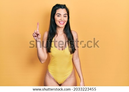 Young hispanic girl wearing swimsuit pointing finger up with successful idea. exited and happy. number one. 